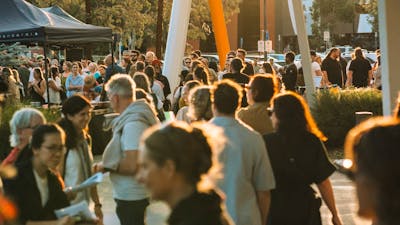 Bustling outdoor crowd at walking at sunset with marquees in the background.
