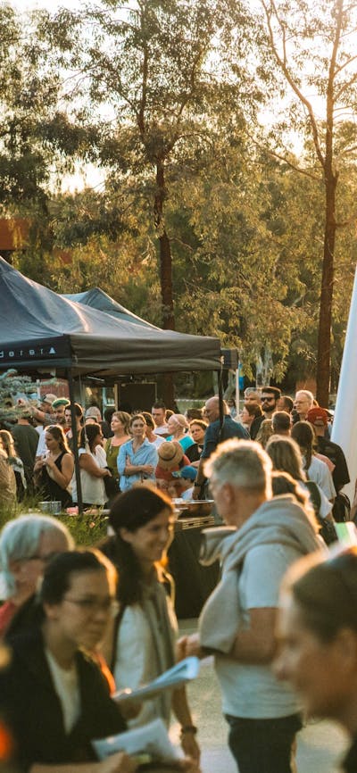 Bustling outdoor crowd at walking at sunset with marquees in the background.
