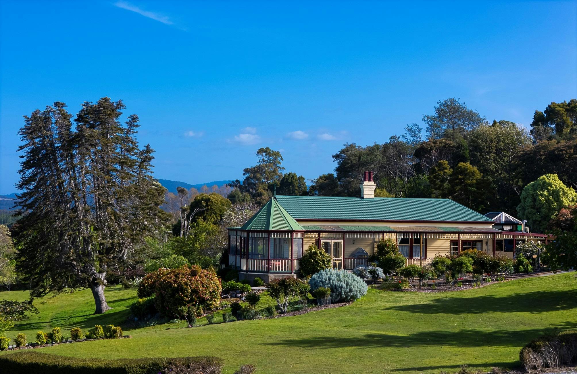 Green lawns, stately gardens and a heritage home against a blue sky.