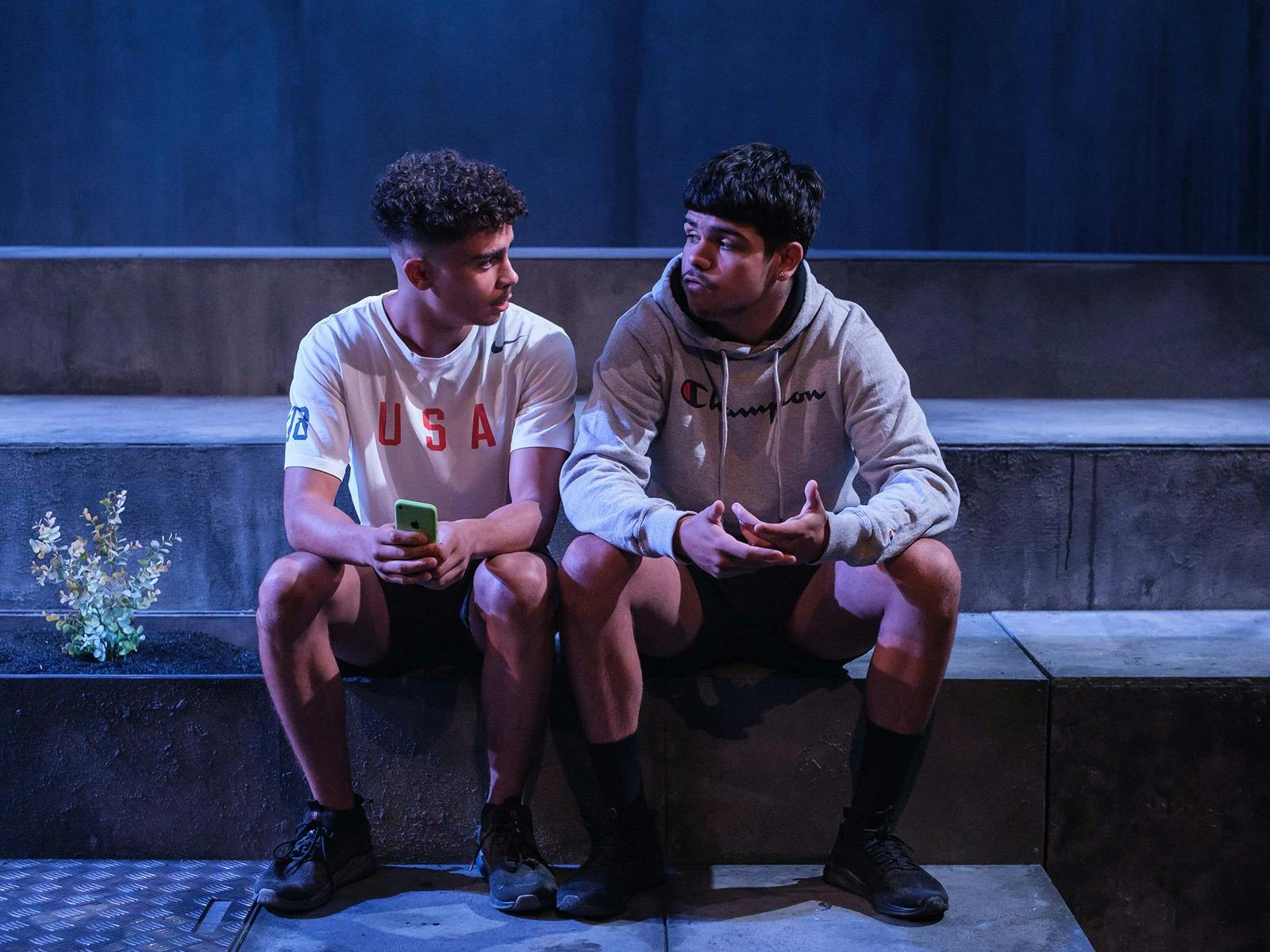 Two young First Nations men sit on a step talking