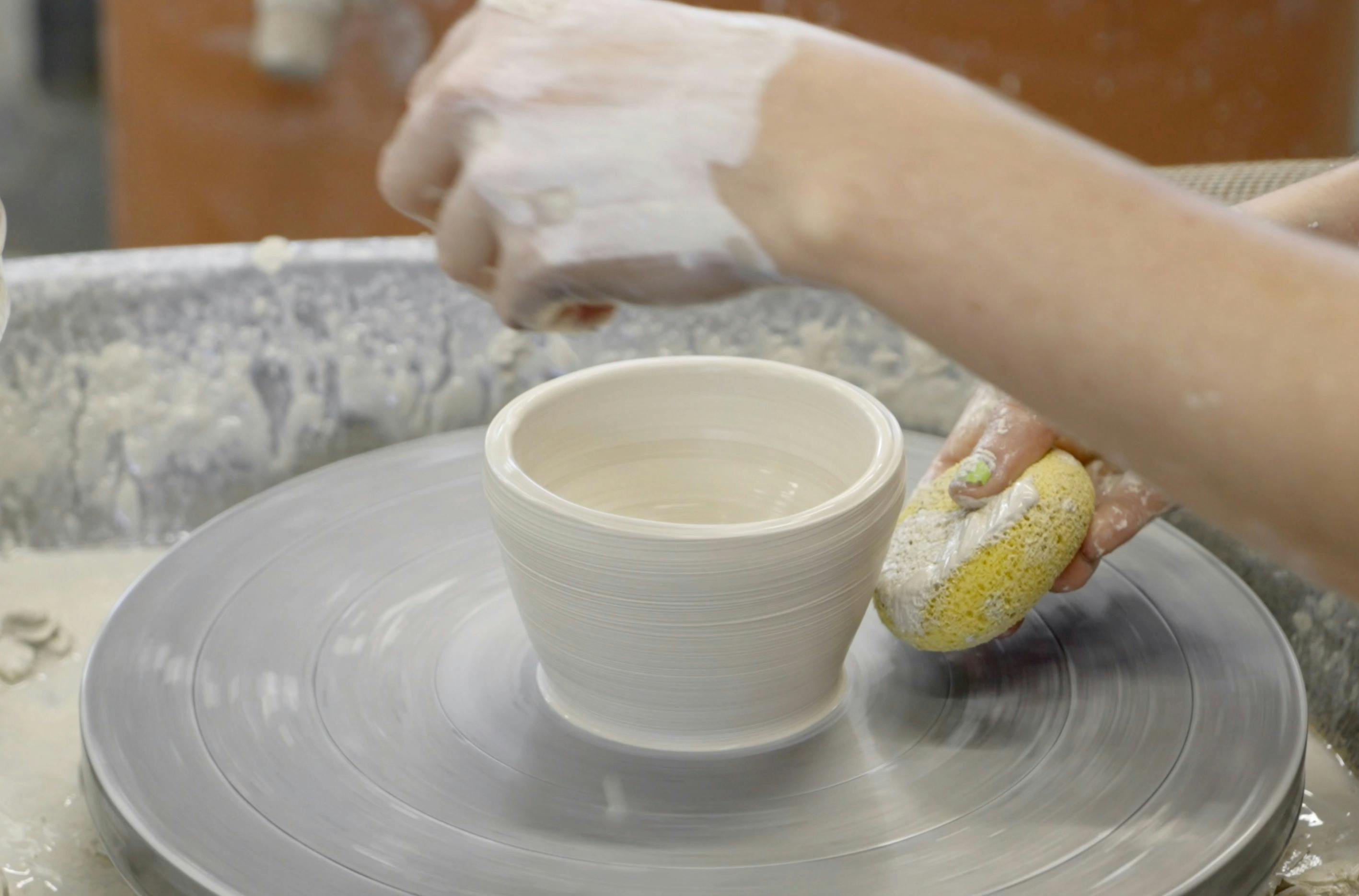 Photograph of hand adding water to clay bowl on a pottery wheel.