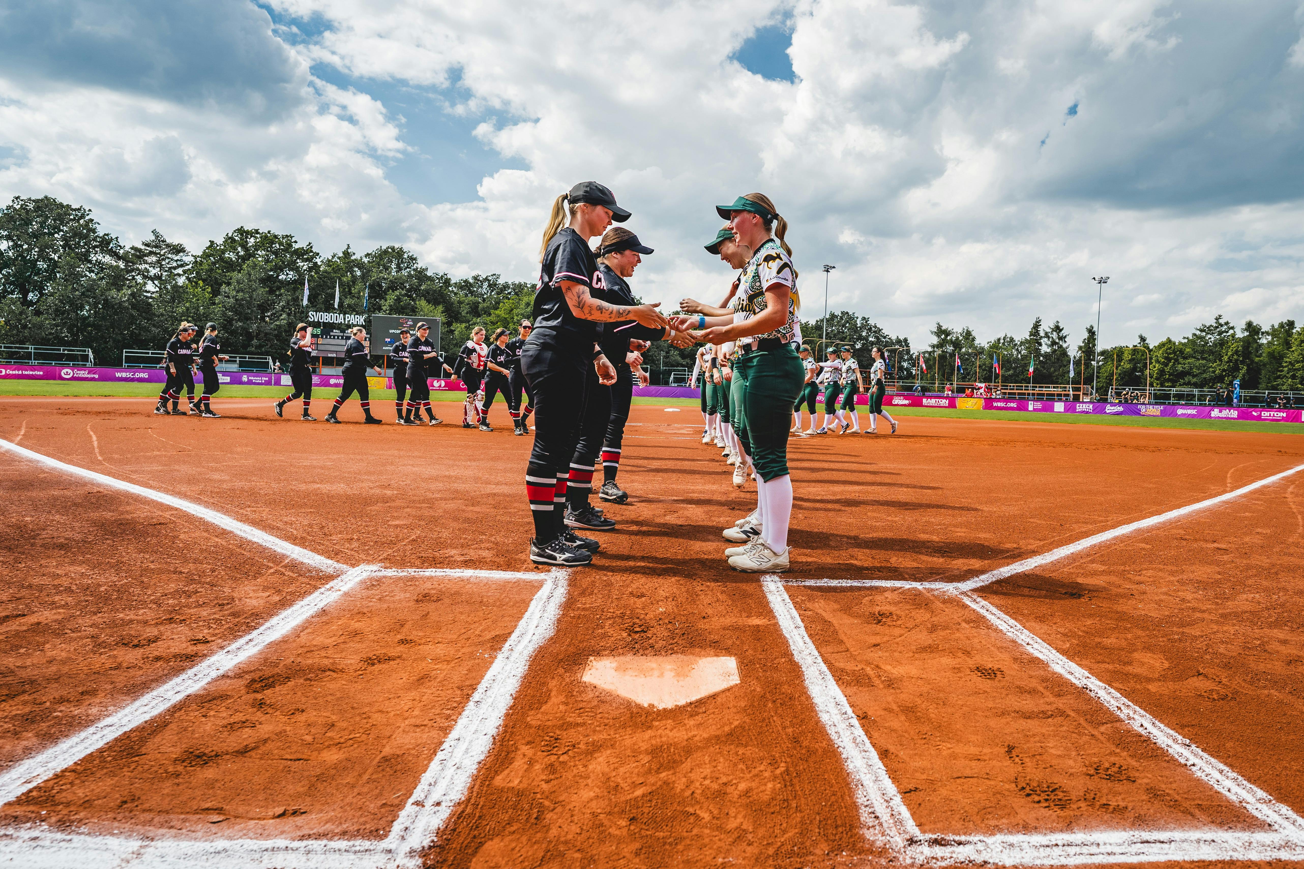 Opposing softball teams shake hands at home plate after a match on a sunny competition field.