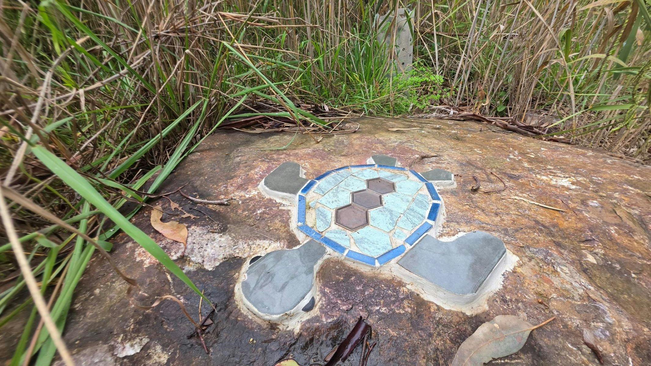 A grey and blue mosaic turtle on a granite rock surrounded by grass