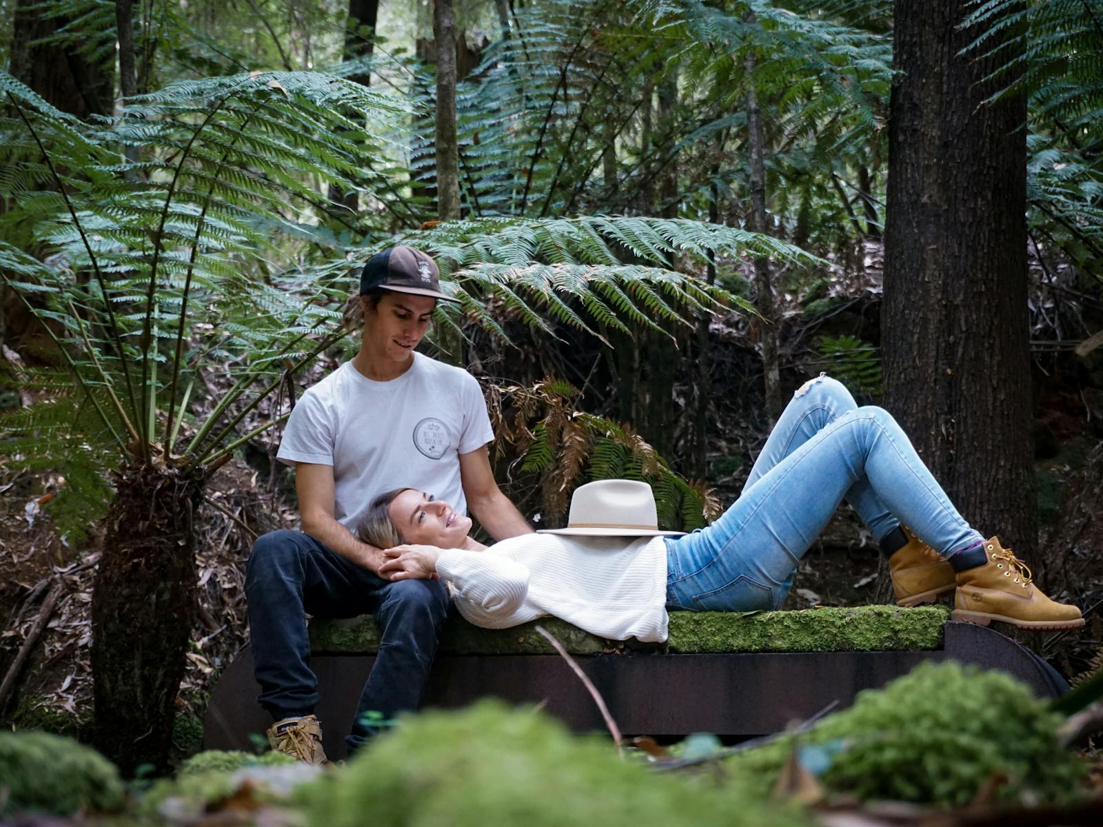 A young couple lying on a stone bench surrounded by tree ferns