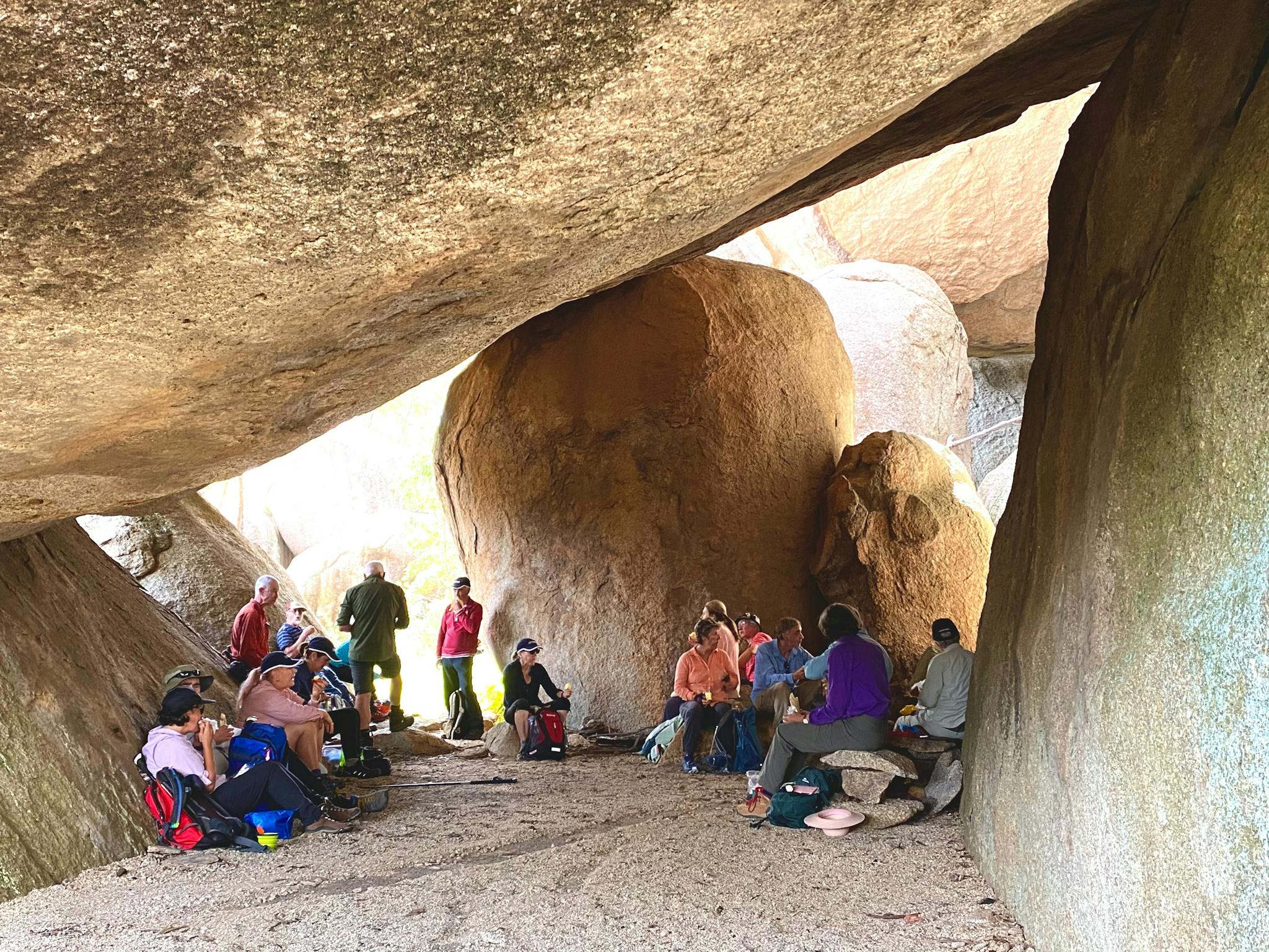 group of adults under a huge boulder