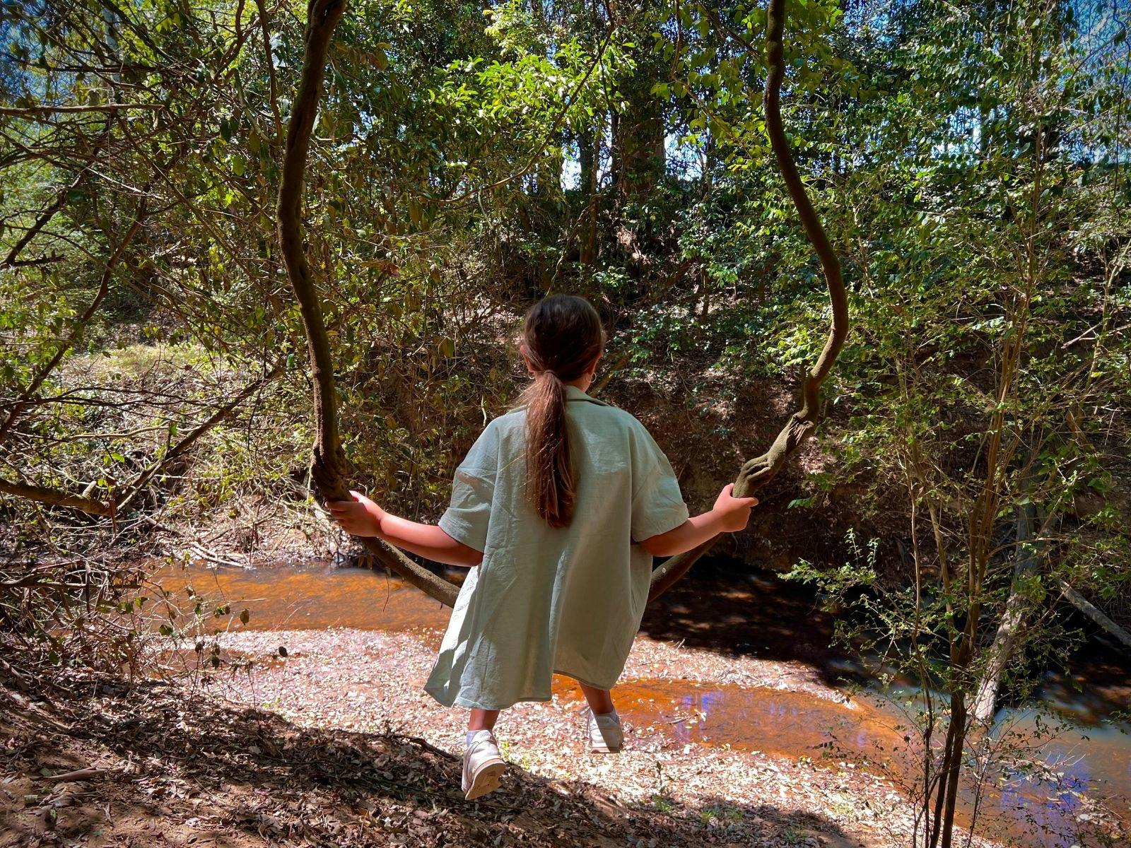 Young girl swinging happily from low tree branches surrounded by greenery