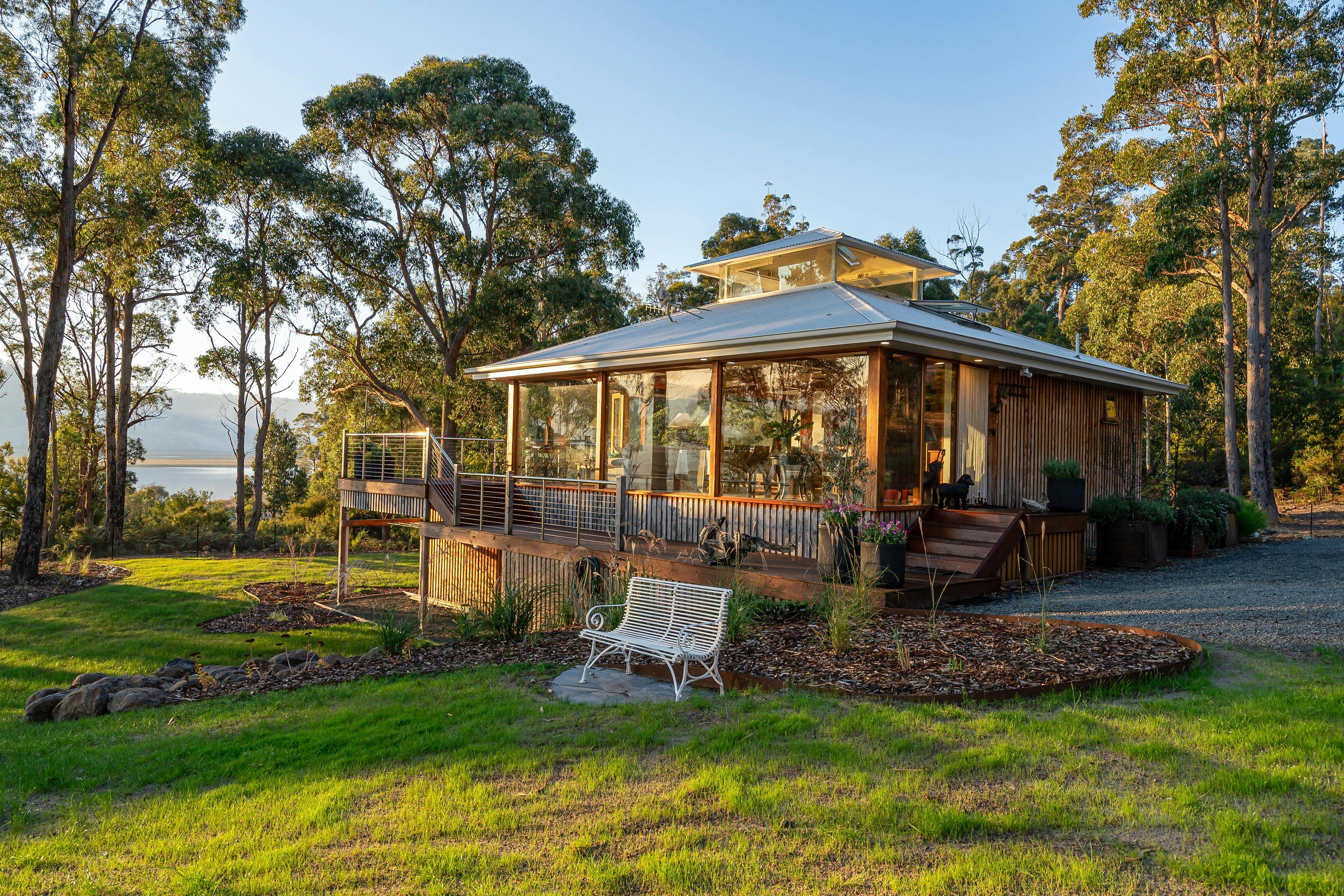 An exterior shot of the Huon River Hideaway bathed in sunlight nestled between gum trees