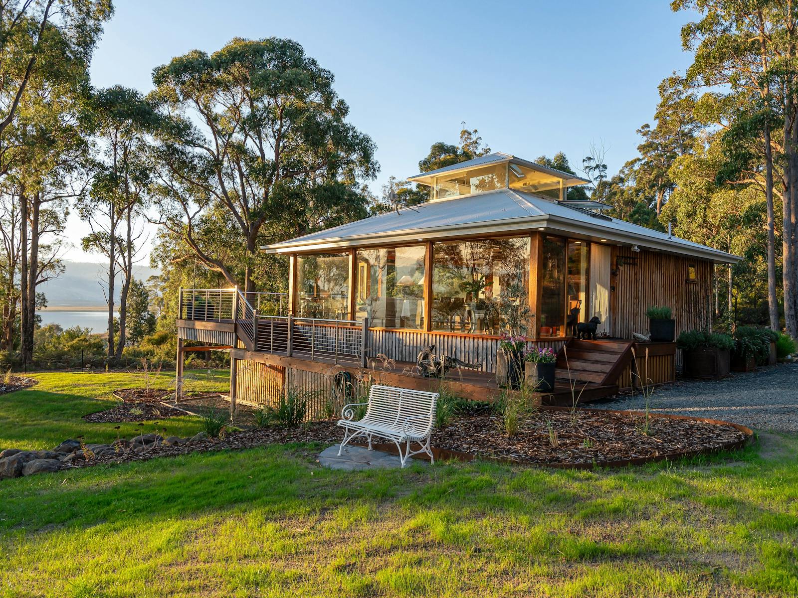 An exterior shot of the Huon River Hideaway bathed in sunlight nestled between gum trees