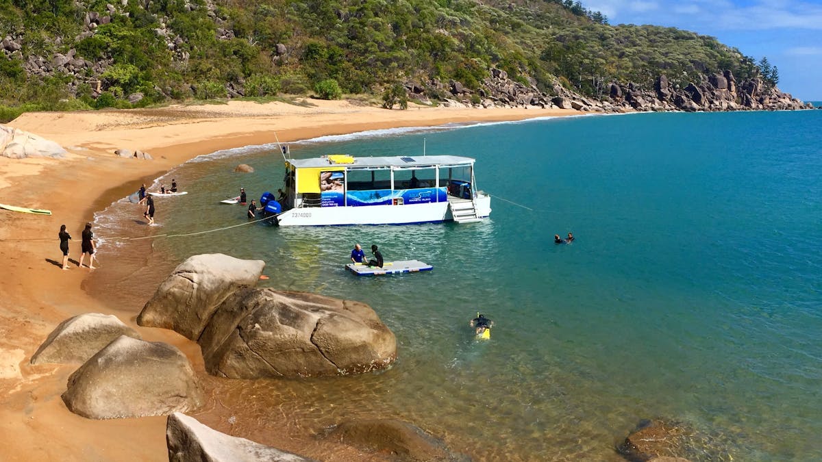 boat at edge of beautiful sandy beach with people swimming in blue ocean, people walking on beach