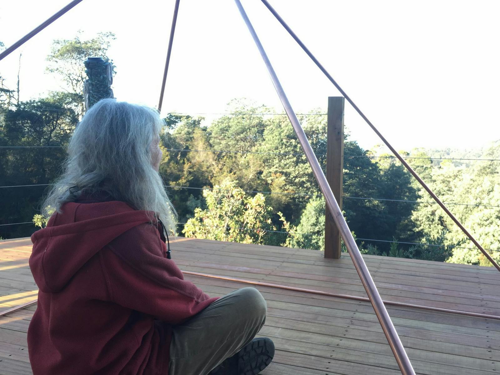 woman sitting under a copper pyramid looking out to the sea