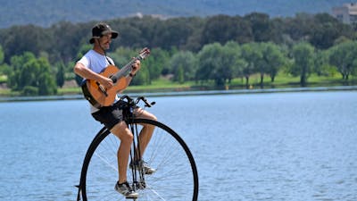 Simon playing a guitar while riding his penny-farthing