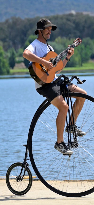Simon playing a guitar while riding his penny-farthing