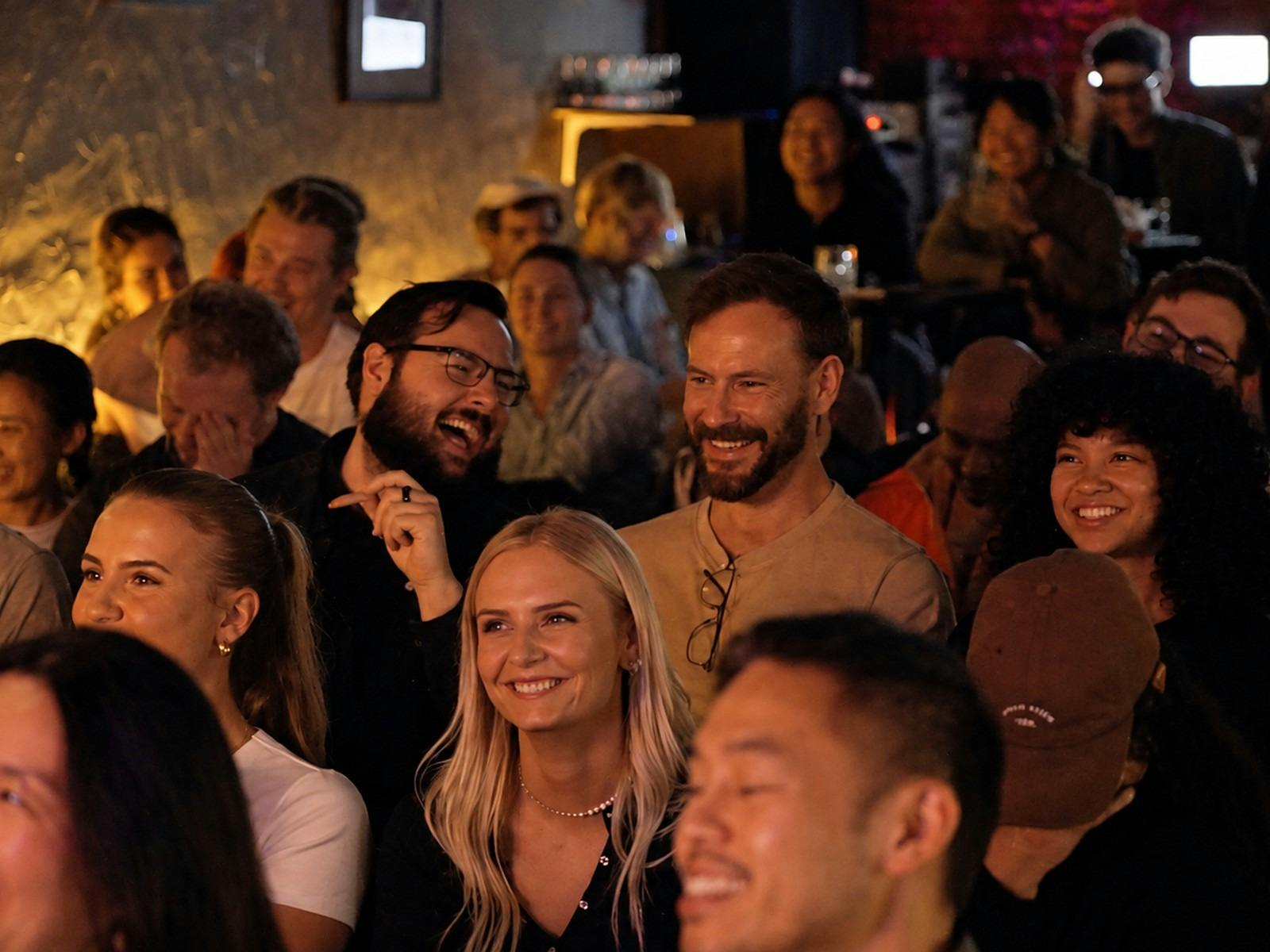 A full room of people seated in rows laughing at a comedy show
