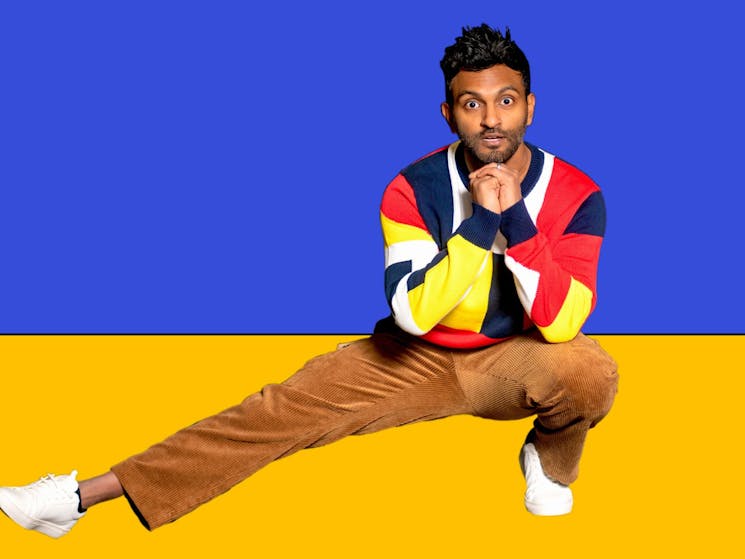 Man crouching with right leg extended out in front of blue and yellow backdrop