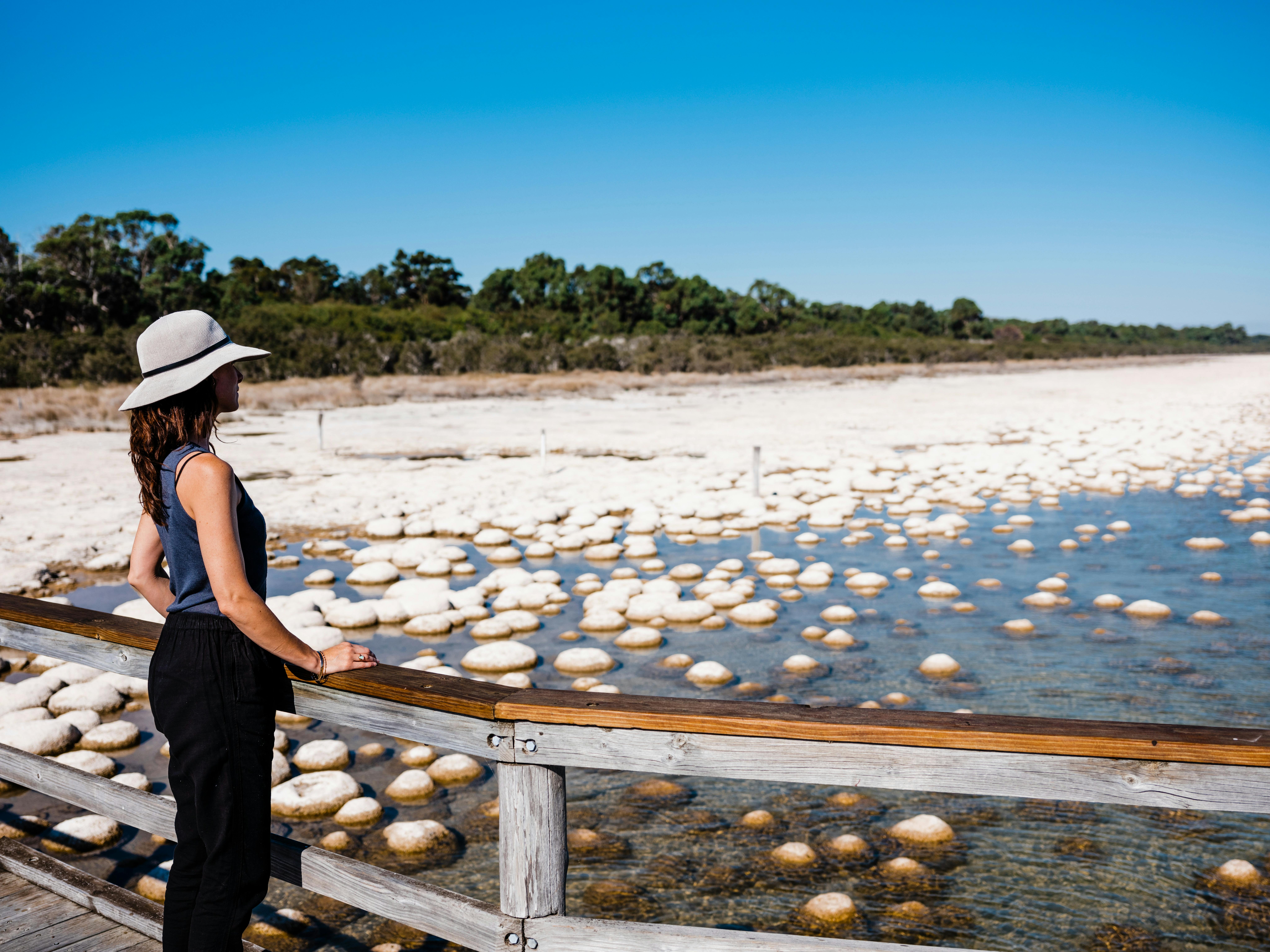 Lady standing on a jetty looking looking out to a reef of thrombolites, unique egg -like rock forms