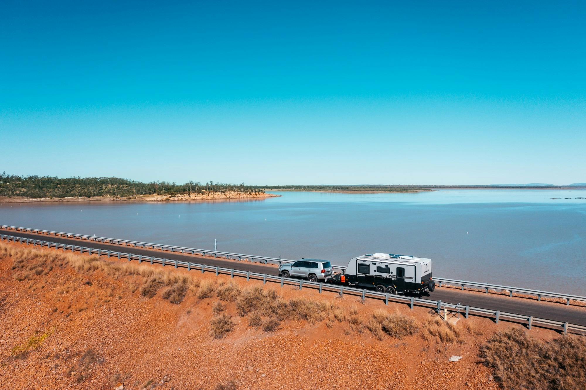 Car towing caravan driving along a road next to large body of water