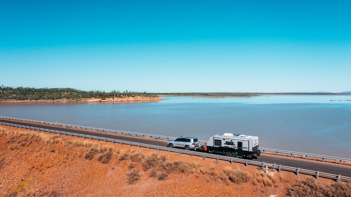 Car towing caravan driving along a road next to large body of water