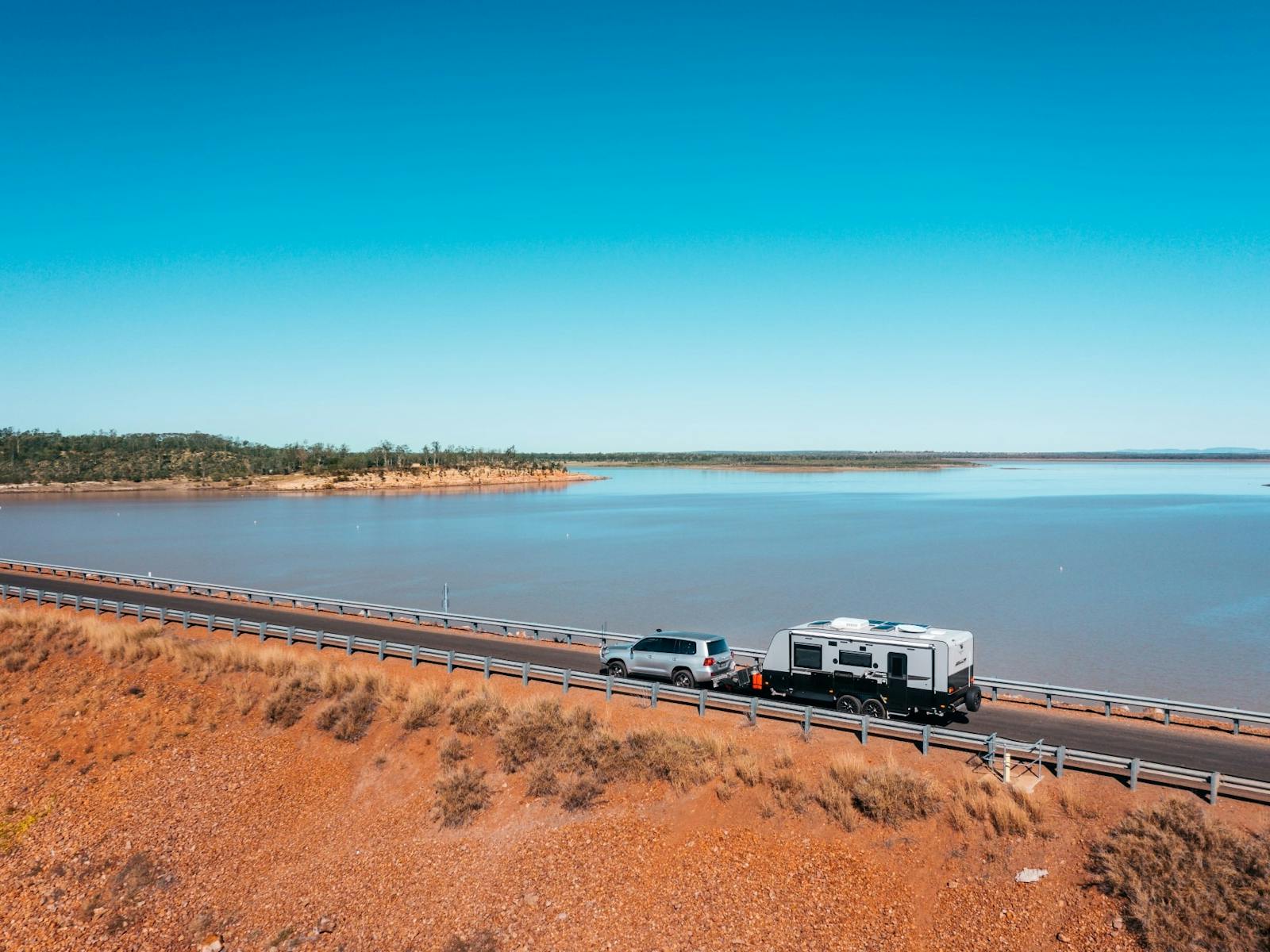 Car towing caravan driving along a road next to large body of water