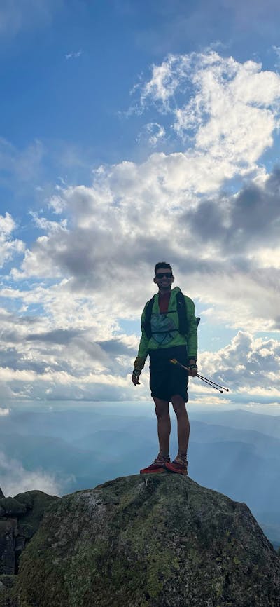 A hiker standing on a rock with clouds behind them.