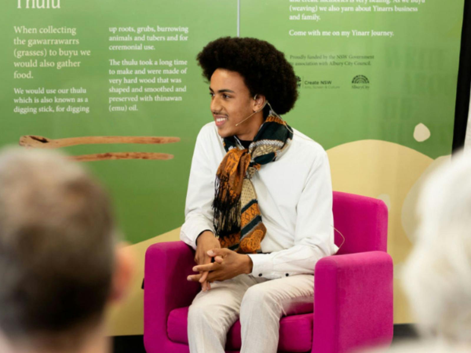 Speaker sitting in a pink armchair presenting on stage in front of an audience.