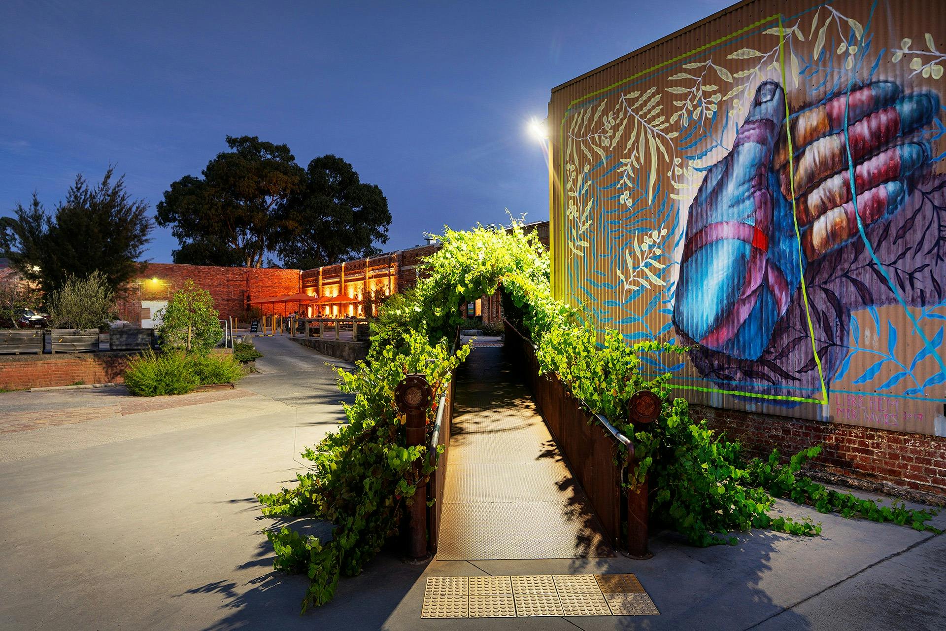 night time showing vine covered walkway leading to Vintage Bazaar & Taproom, and street art mural