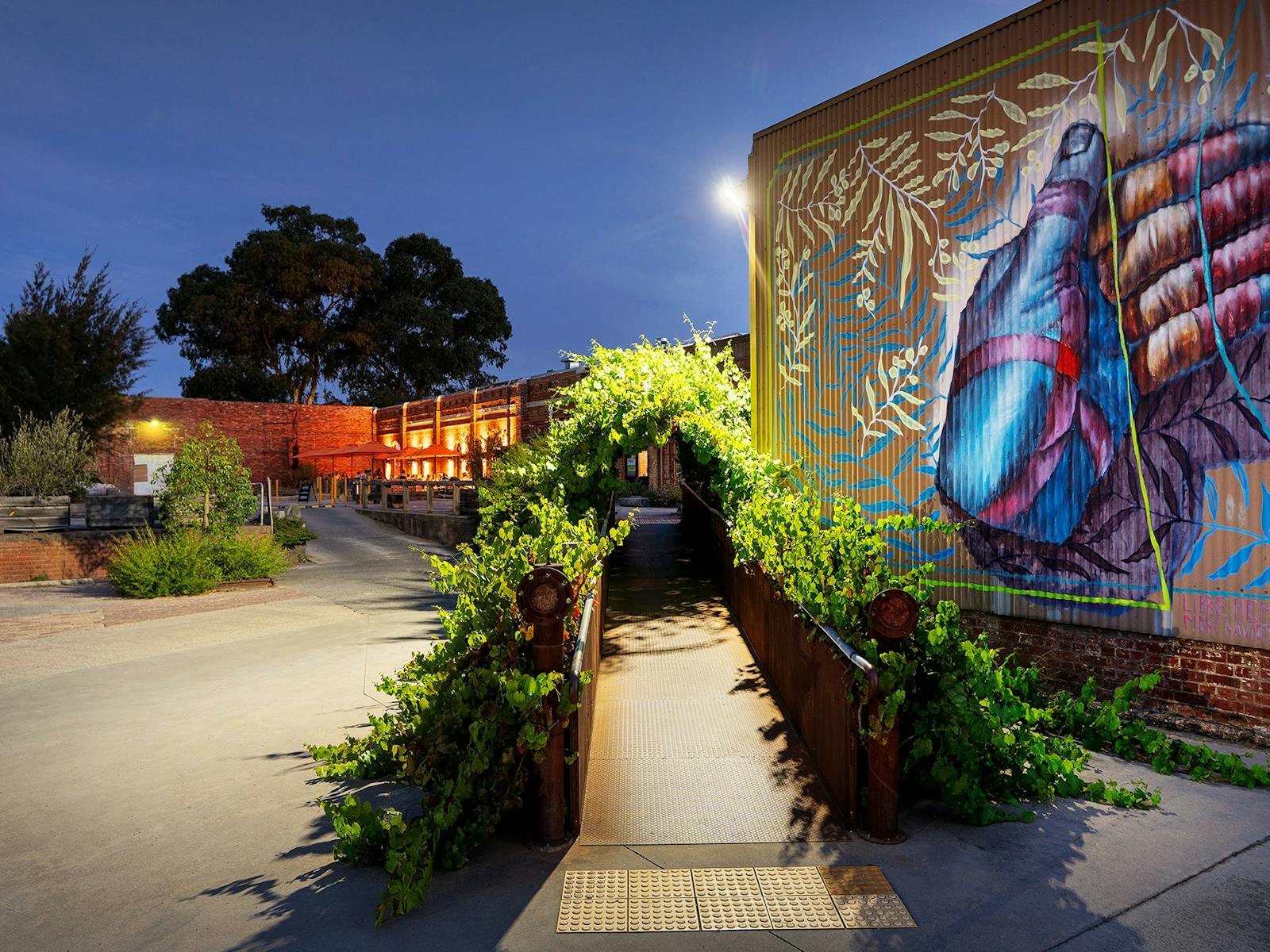 night time showing vine covered walkway leading to Vintage Bazaar & Taproom, and street art mural