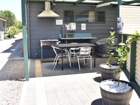 Outdoor BBQ area with rangehood, table and chairs, potted plants and covered patio area with lounge