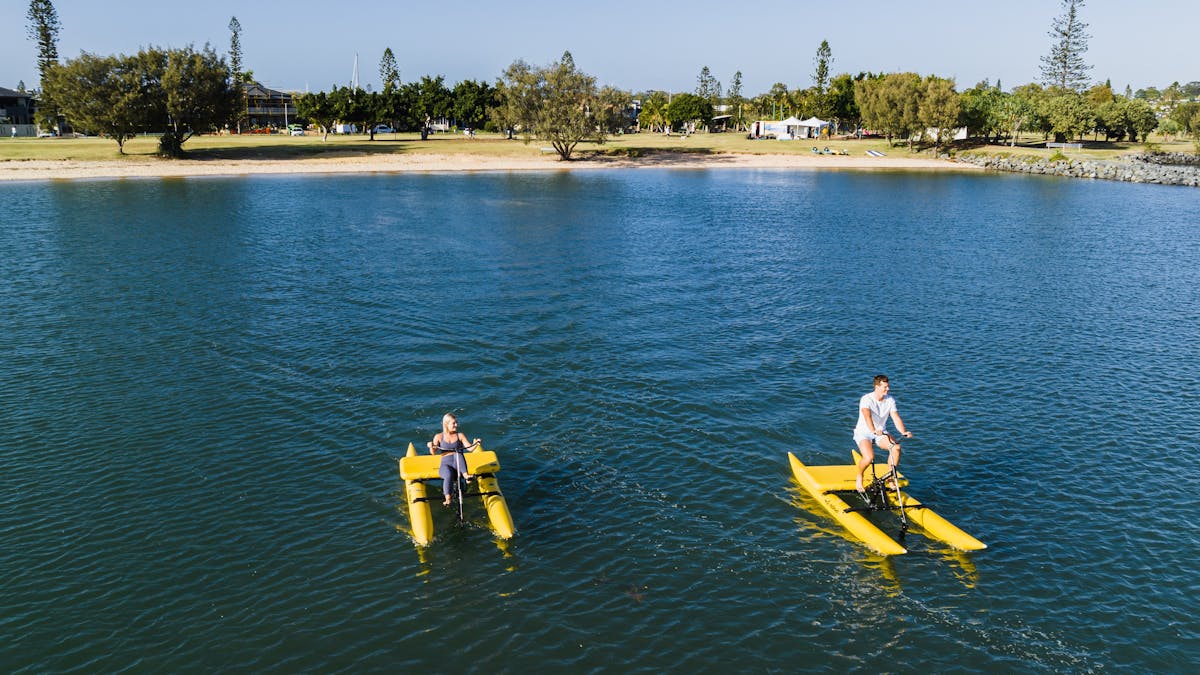 People paddling yellow rowing canoes on the calm blue waters of Raby Bay Foreshore, Redlands Coast,
