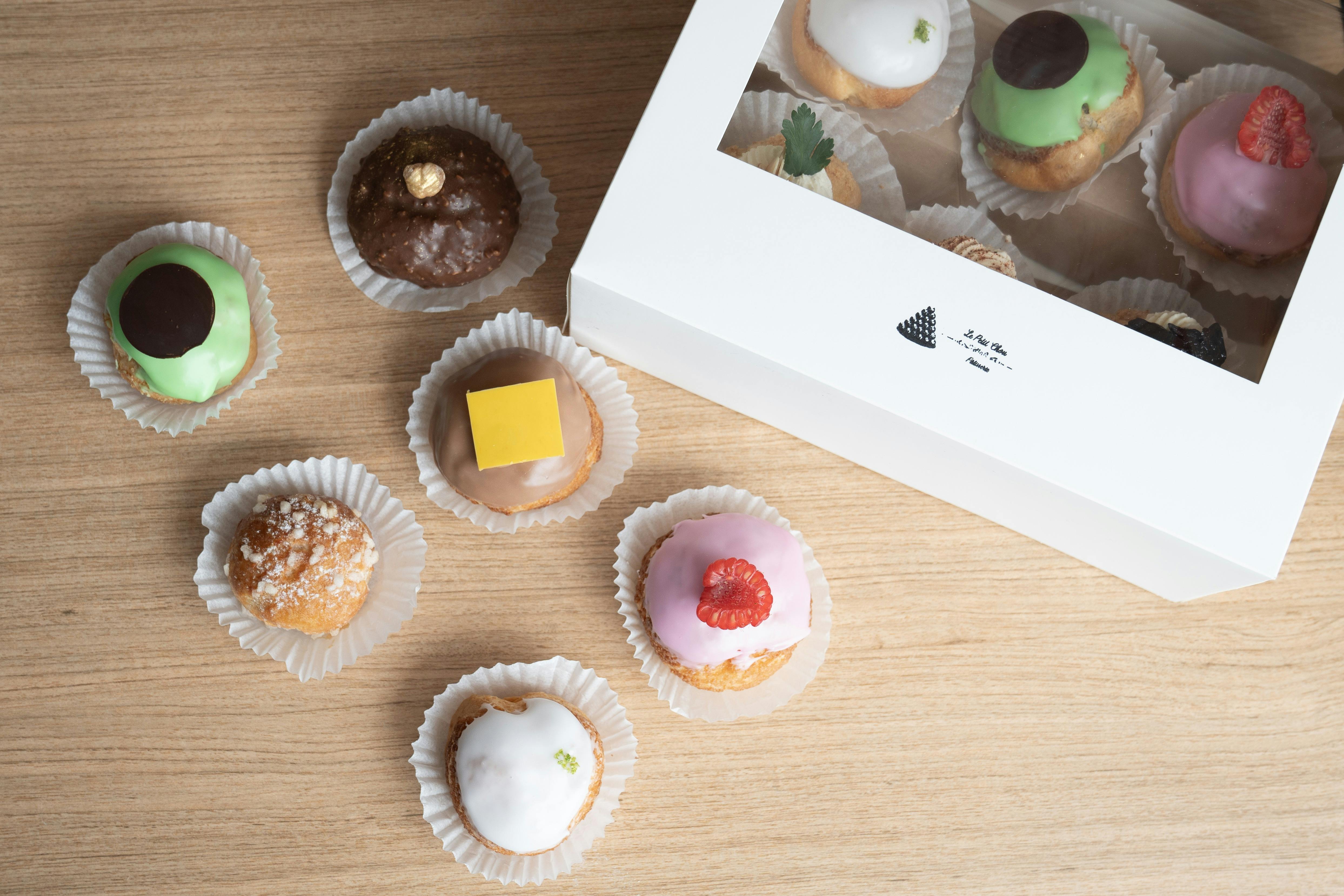 French chou pastries of different colours in a box, and some outside of a box.
