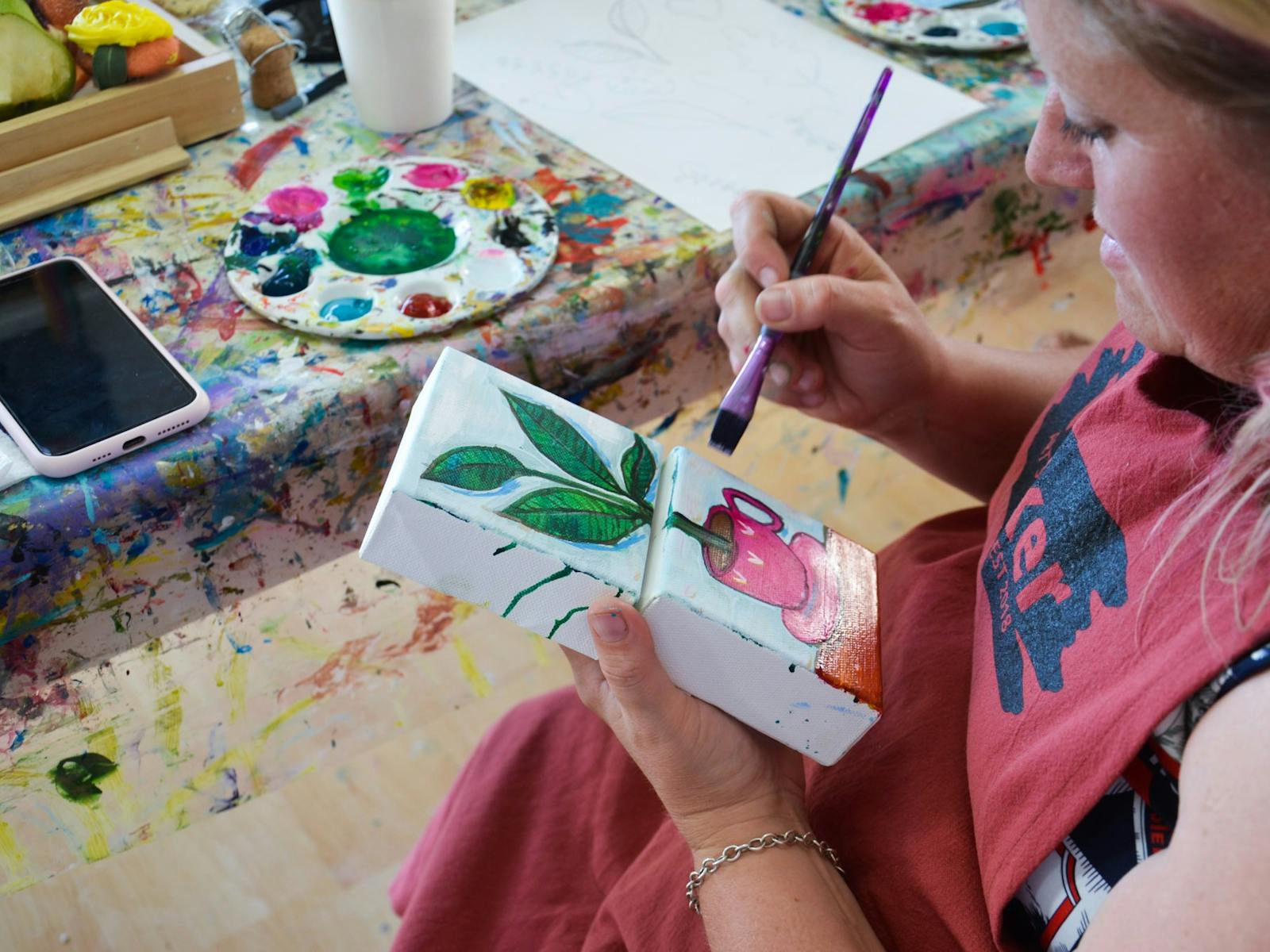 A person painting a picture of a potted plant onto mini canvas