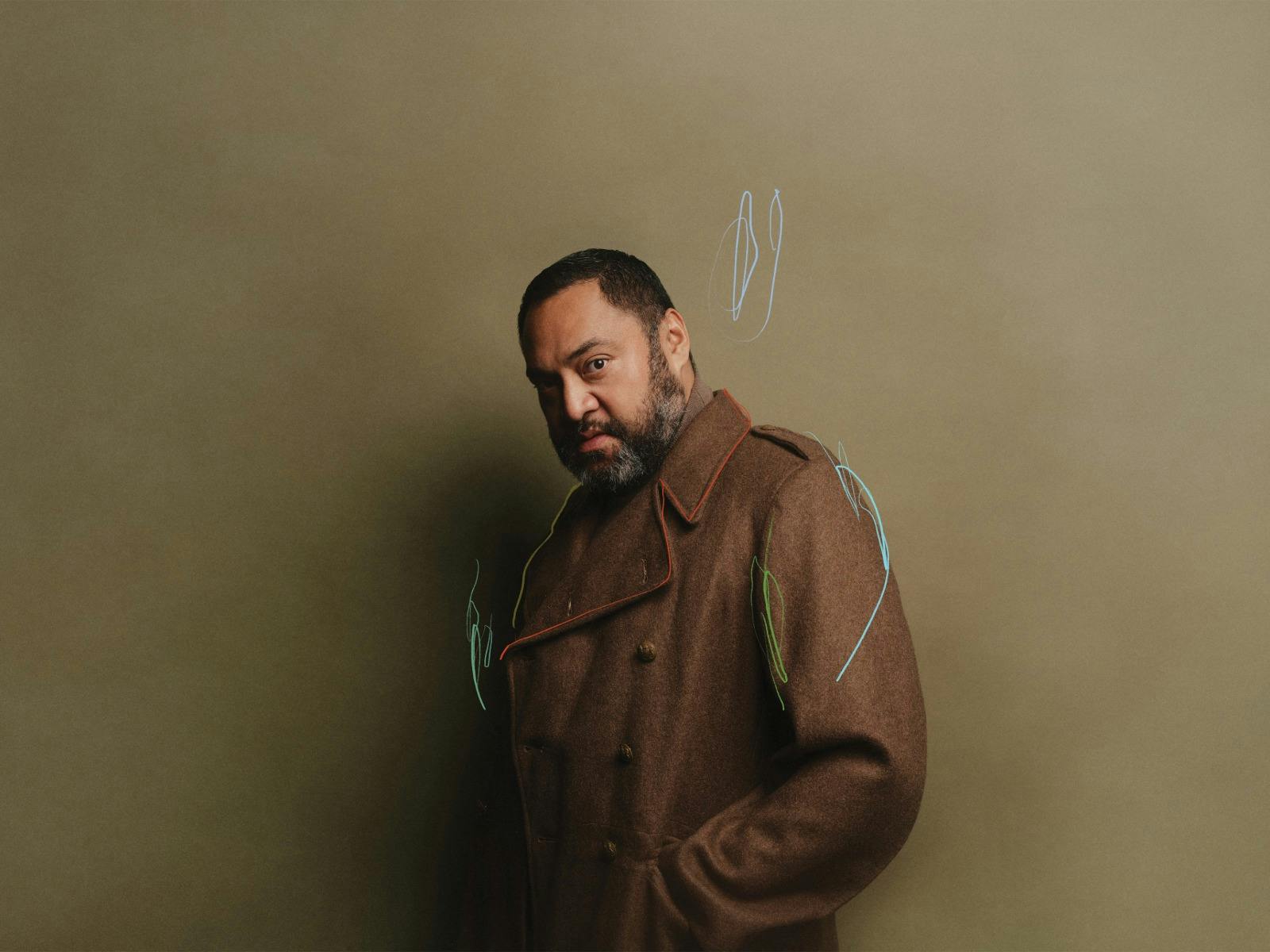 dark skin man in brown jacked standing in front of light brown wall