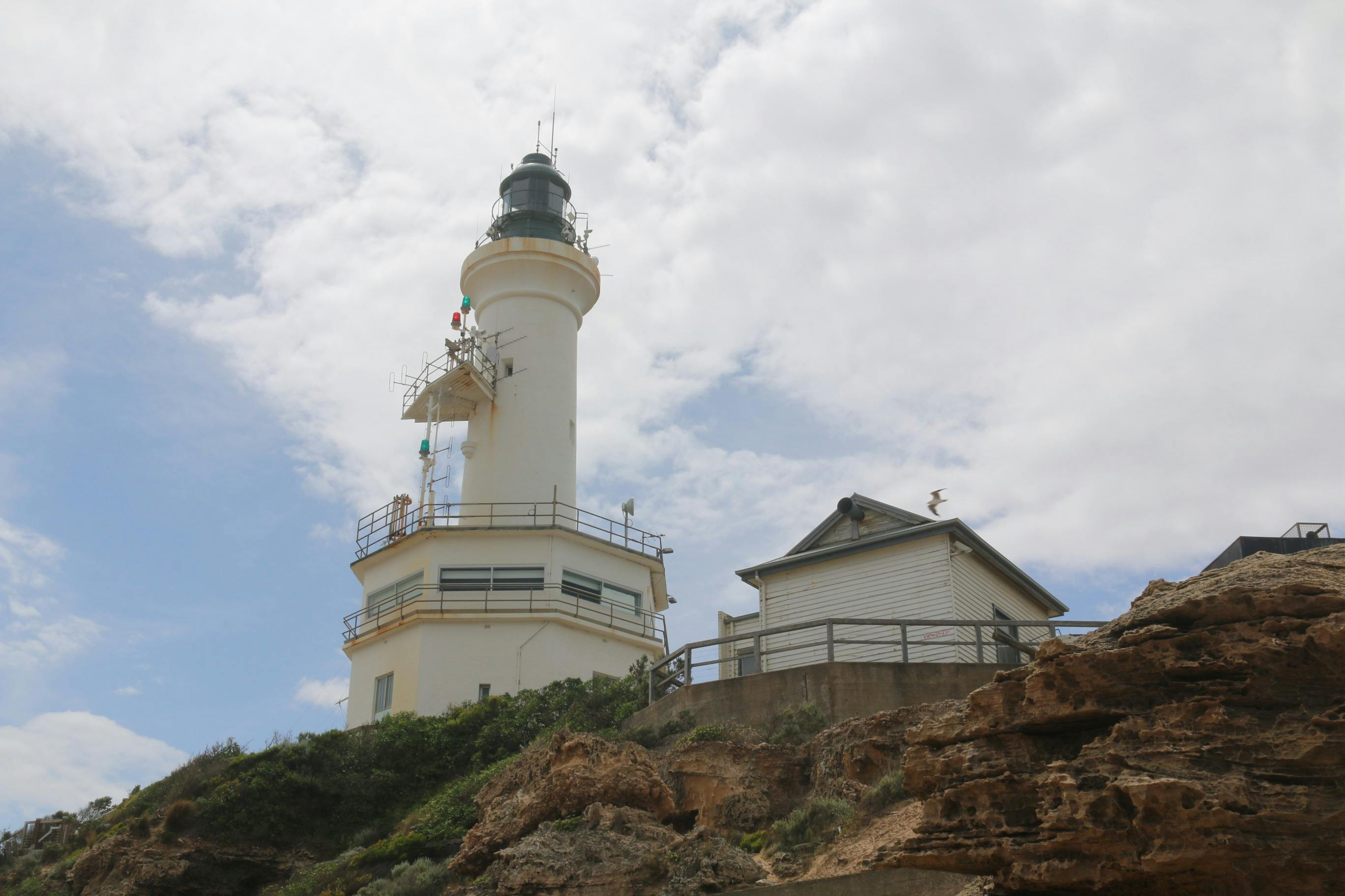 Looking up for the beach at a white lighthouse and a white weatherboard building beside it