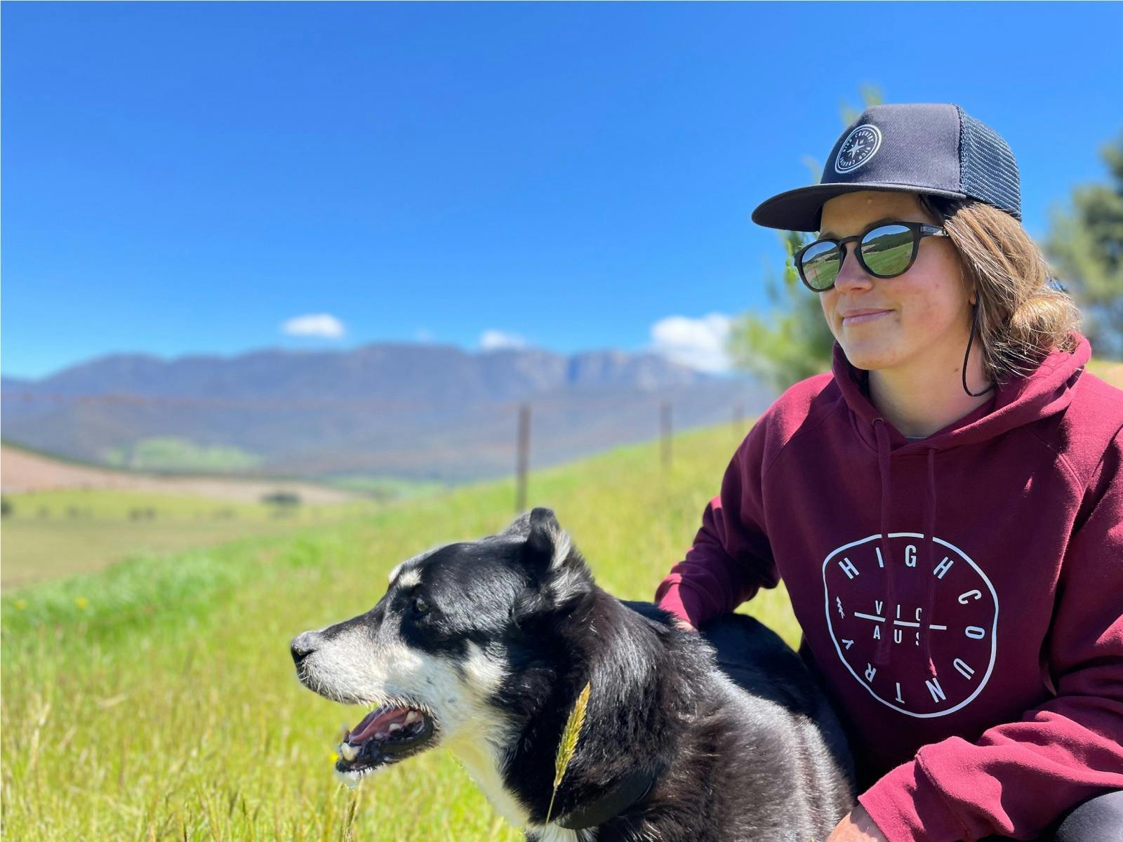 Lady with her dog wearing a high country inspired designed cap and hoodie in front of Mount Buffalo