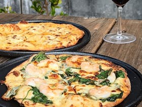 2 pizzas on a wooden table with a glass of red wine