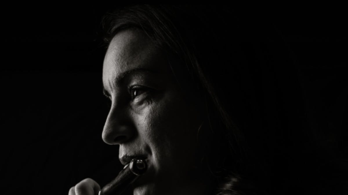 Black-and-white portrait of a piccolo player in profile, looking toward the light