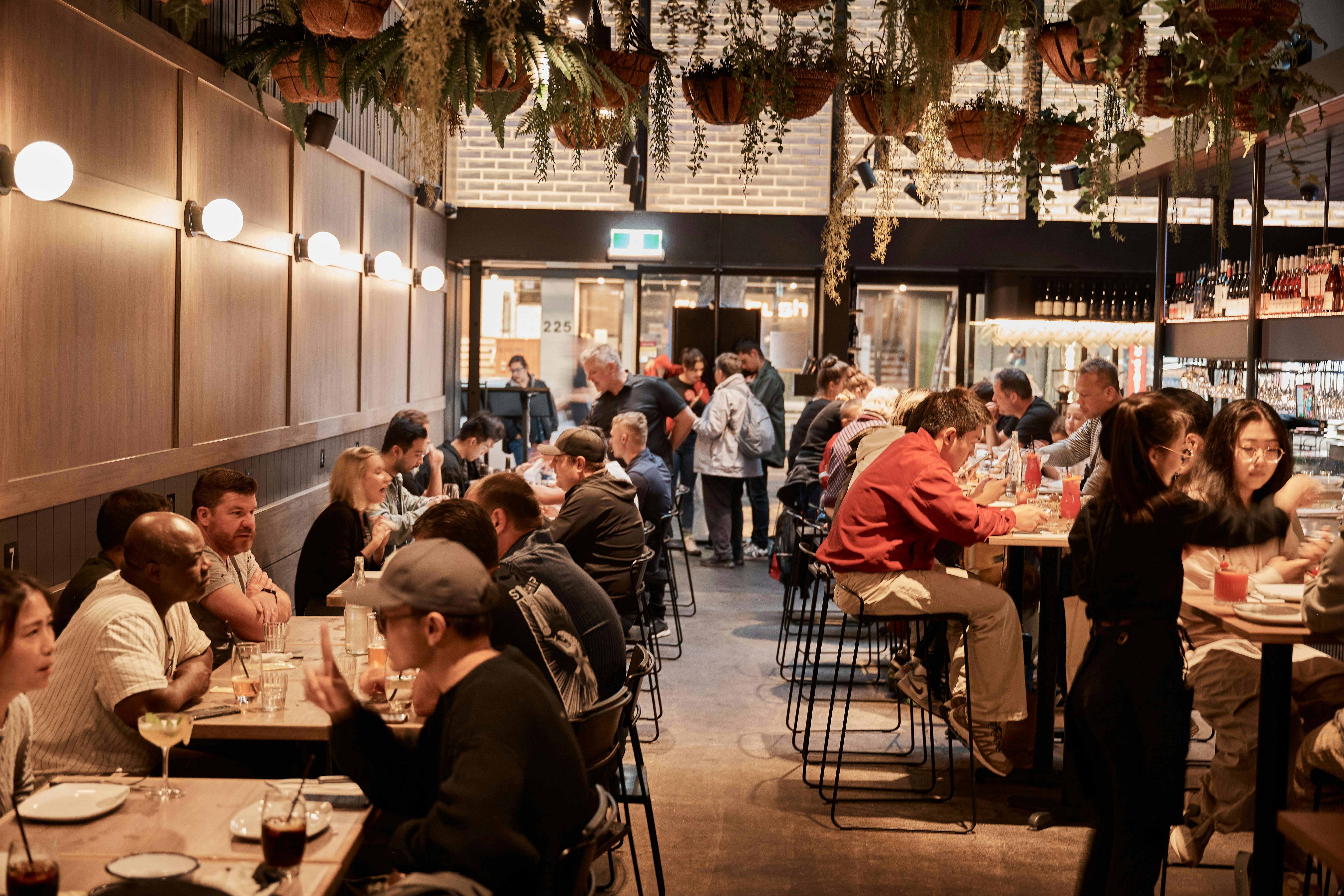 a busy dining room with people sitting along a banquette and at the bar