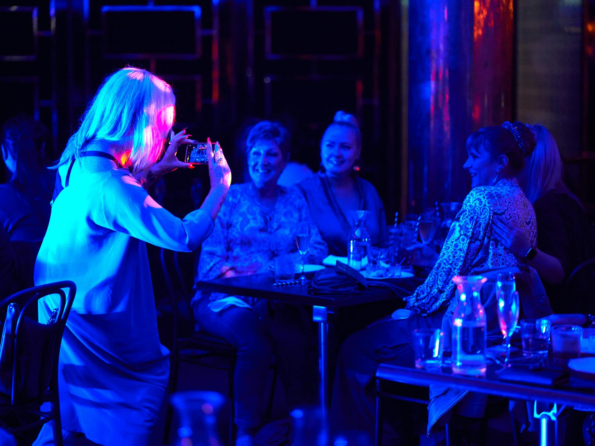 Six mature women taking a photo at their cabaret table to remember their night in Sydney