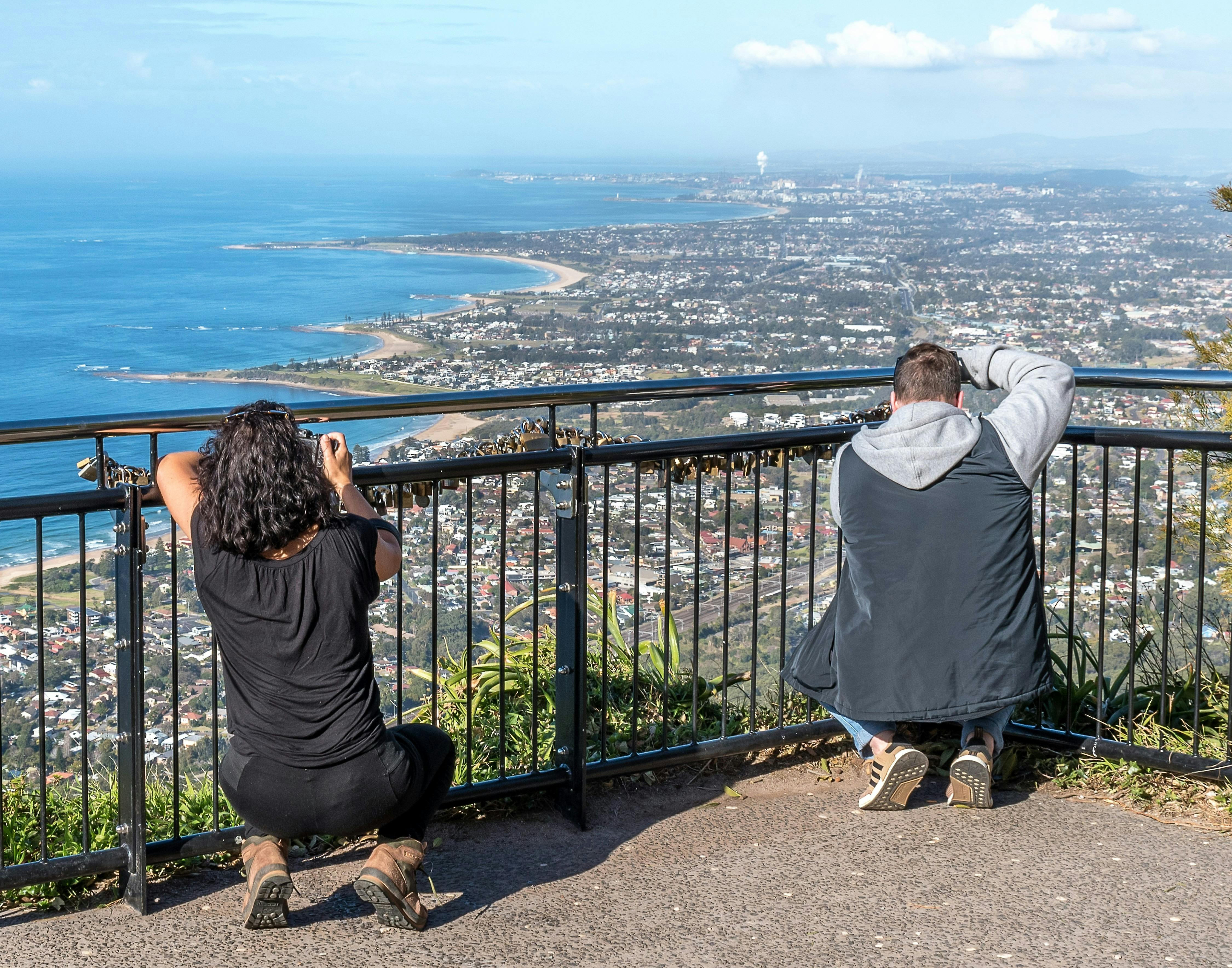 Two people crouch at a barrier fence to photography coasttline distant views