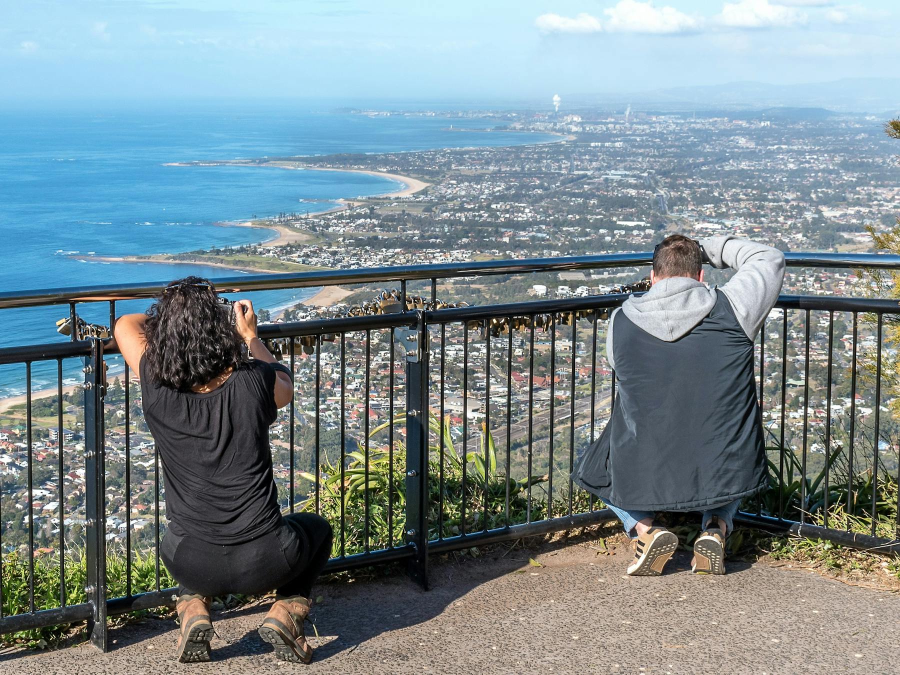 Two people crouch at a barrier fence to photography coasttline distant views