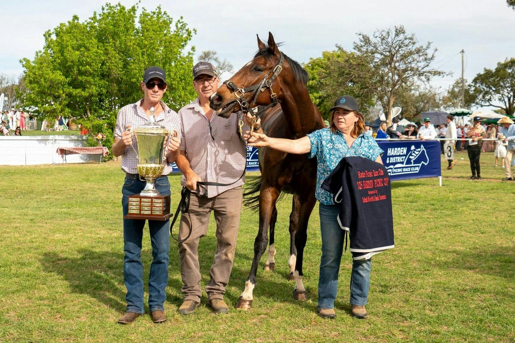 Winner horse with three handlers, one of which is holding a huge trophy prize.