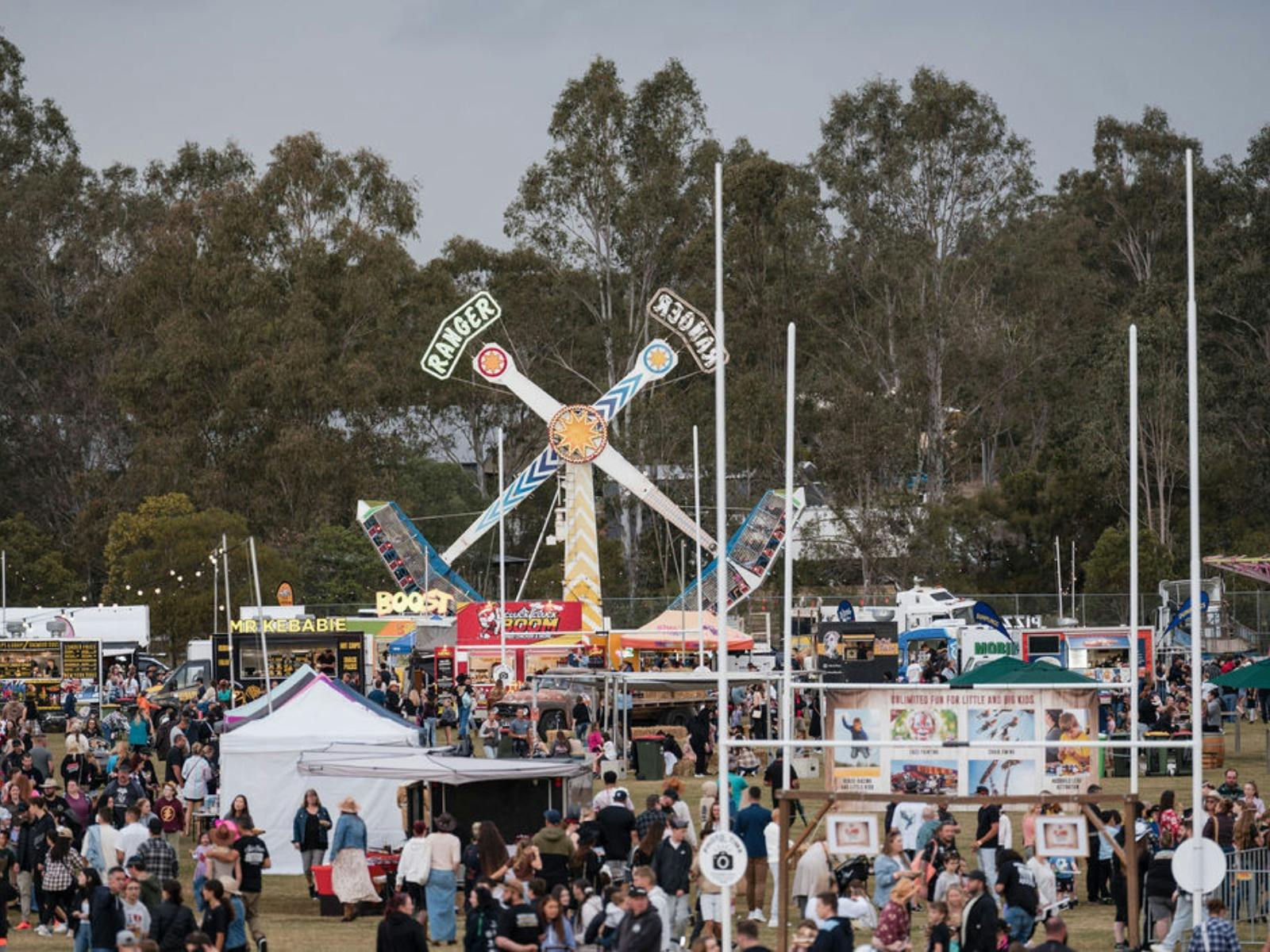 Crowds explore food stalls and carnival rides at a busy outdoor festival