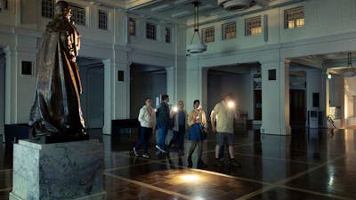 Tim holds a torch and leads a group of people through the dark in King's Hall