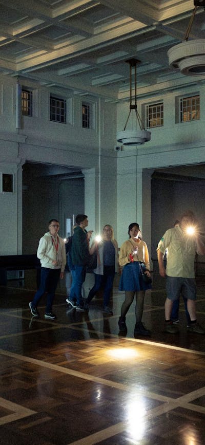 Tim holds a torch and leads a group of people through the dark in King's Hall