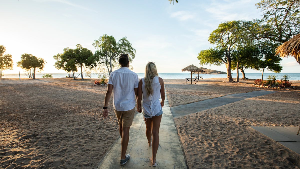 A couple is holding hands and walking along the footpath to the beach during sunset