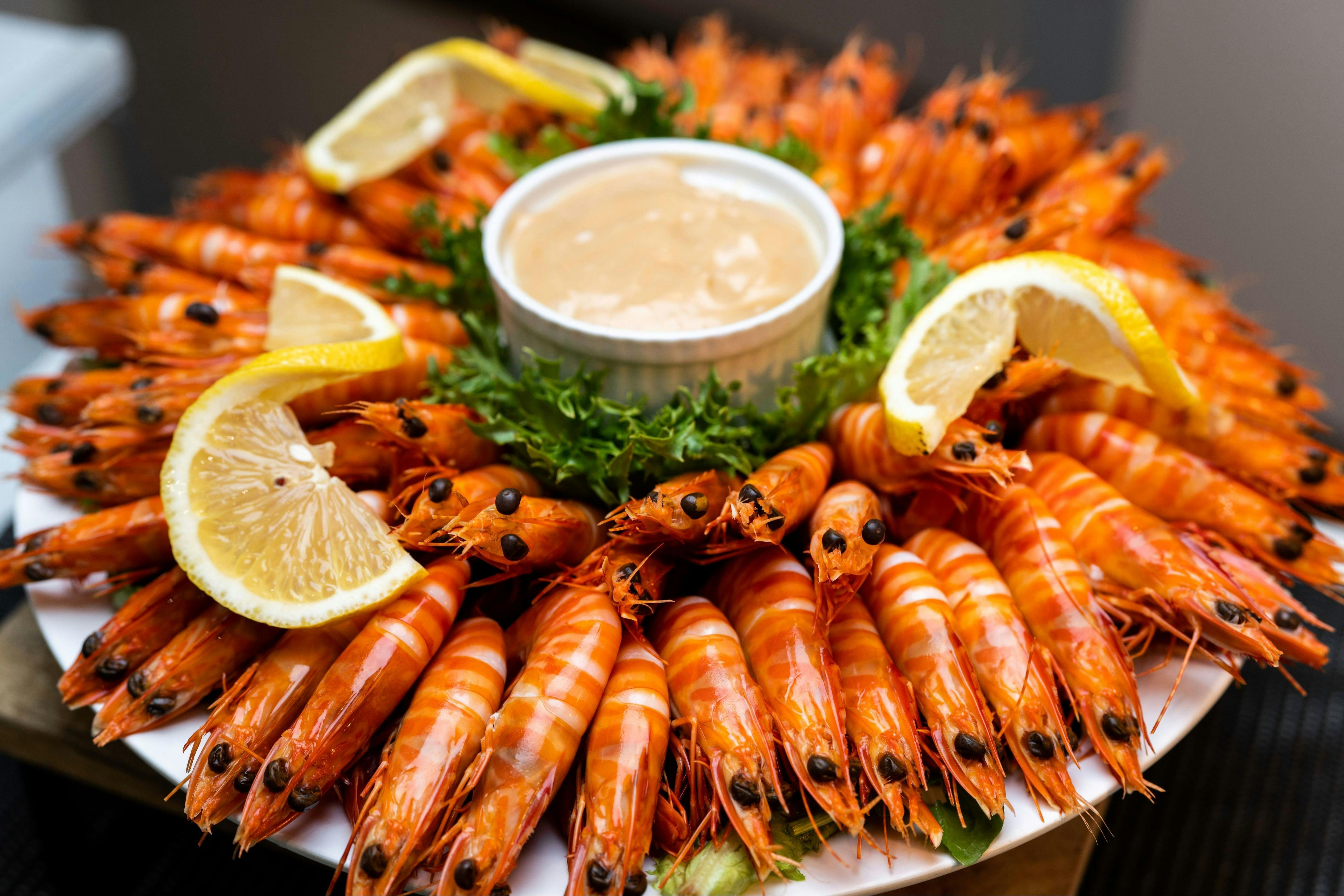 A large platter of cooked prawns arranged in a circular pattern around a central dipping sauce.