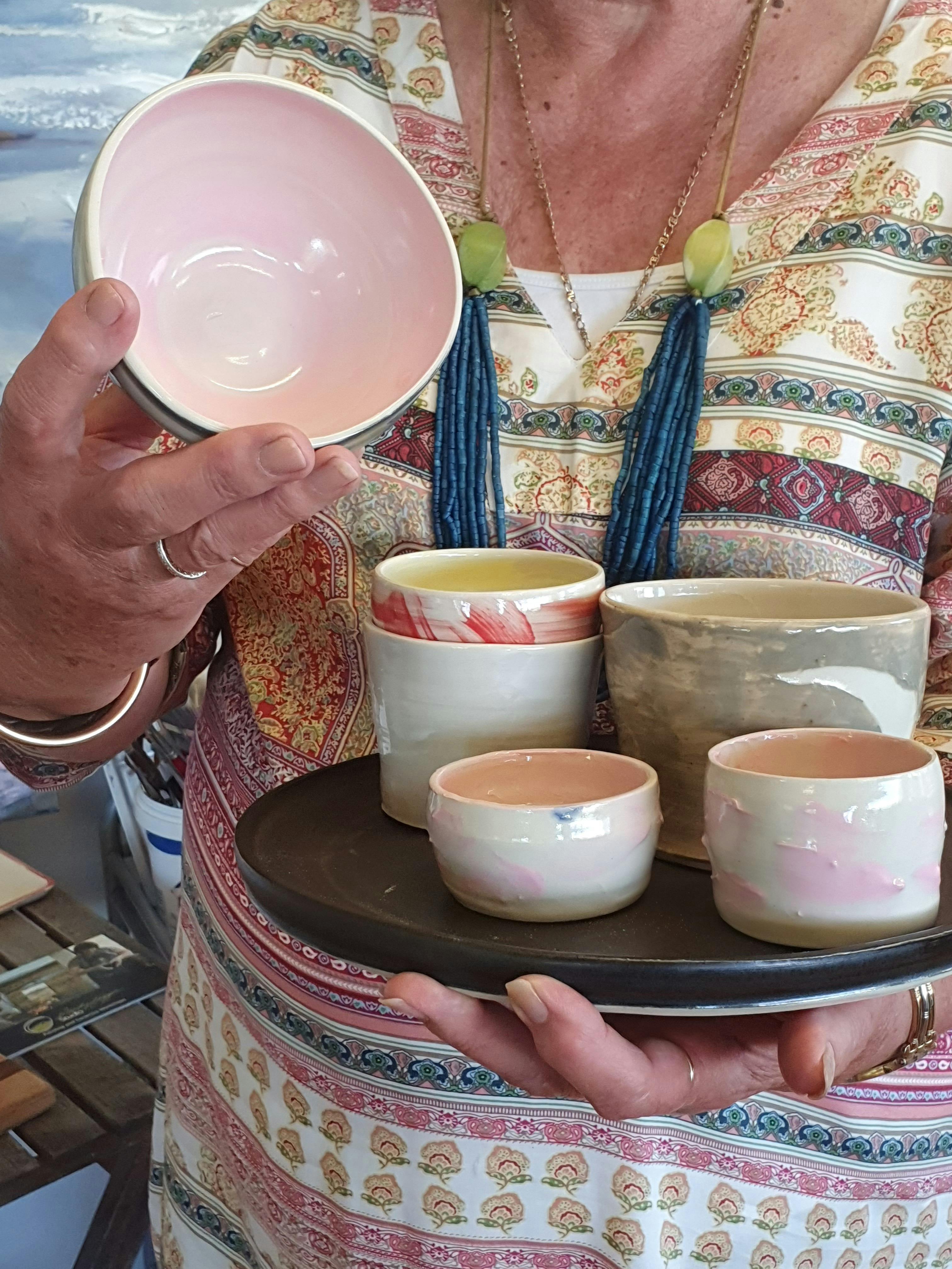 A group of pottery vessels, white with pink decoration held by participant.