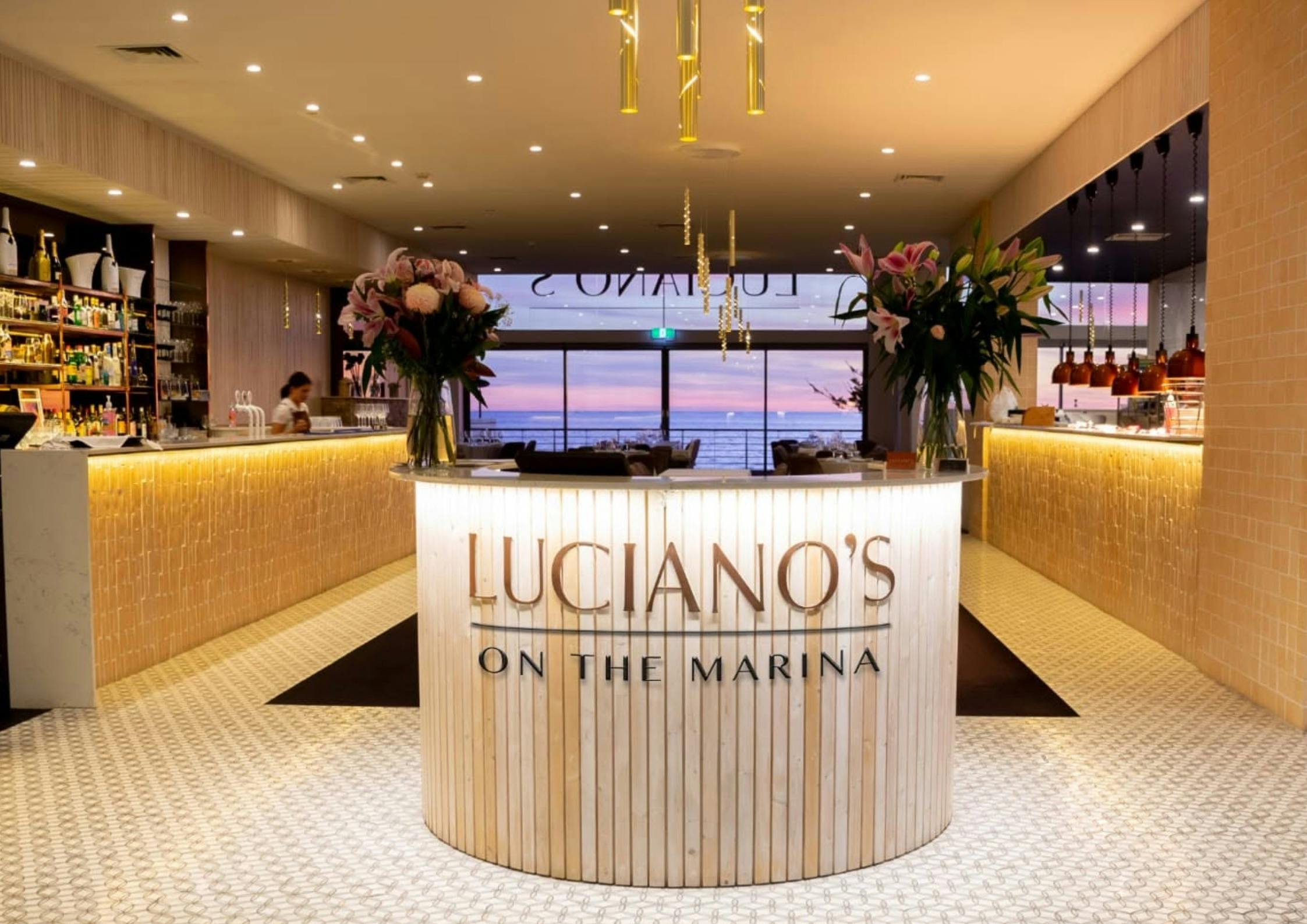A picture of the Luciano's welcome desk with a pink purple sunset behind and the restaurant behind