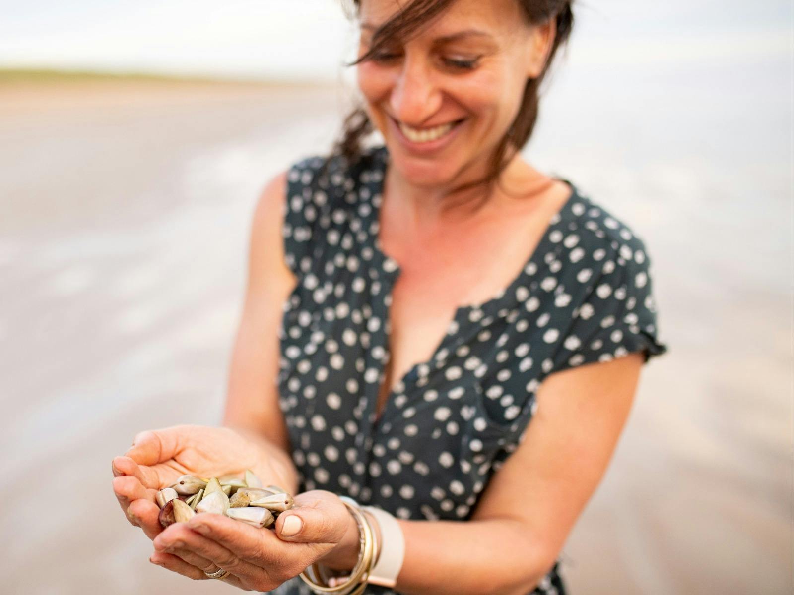 Person holding fresh caught pipi in their hands, Smiling.