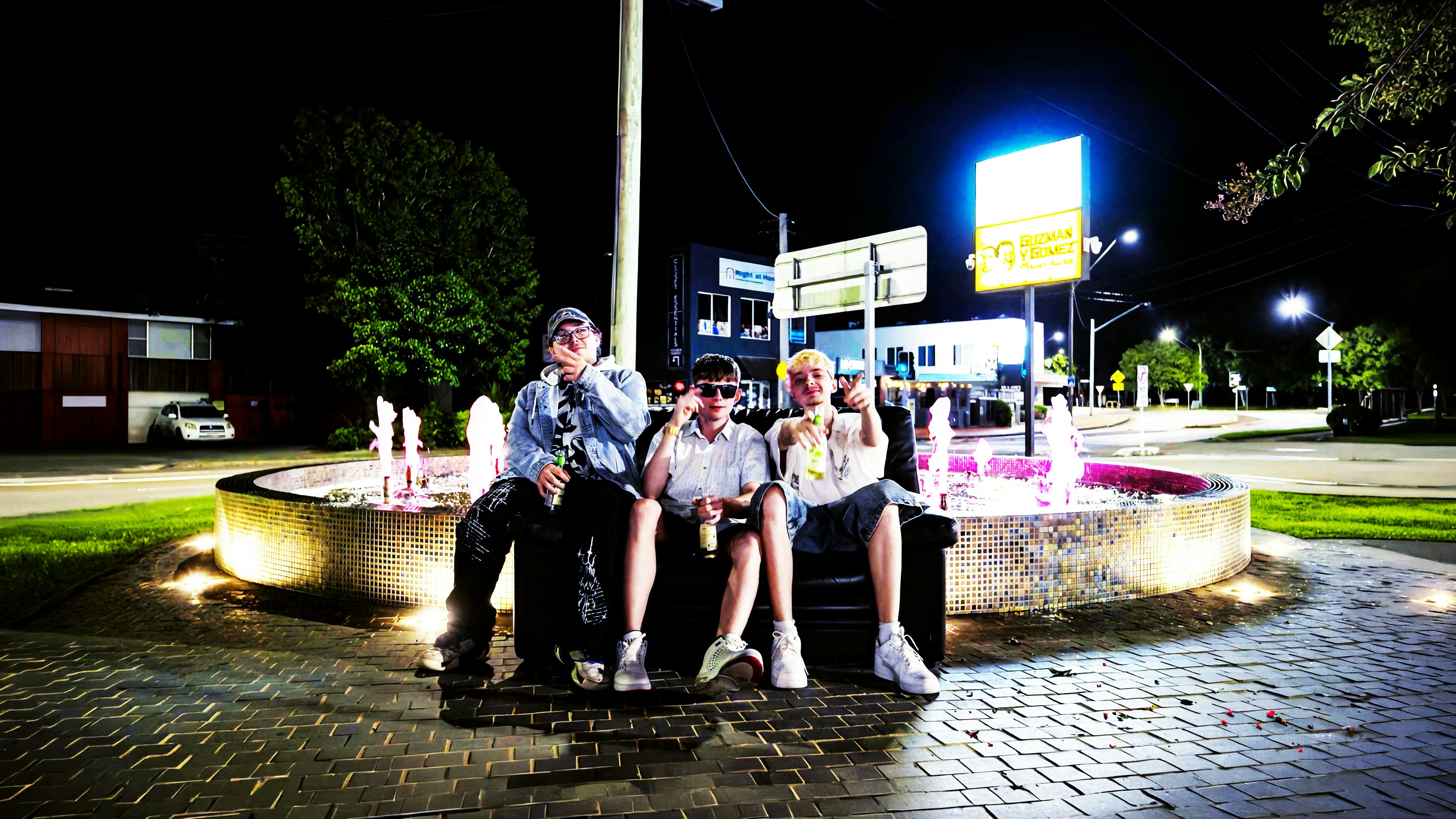 Three young men sitting in front of a fountain at night recreating the friends intro