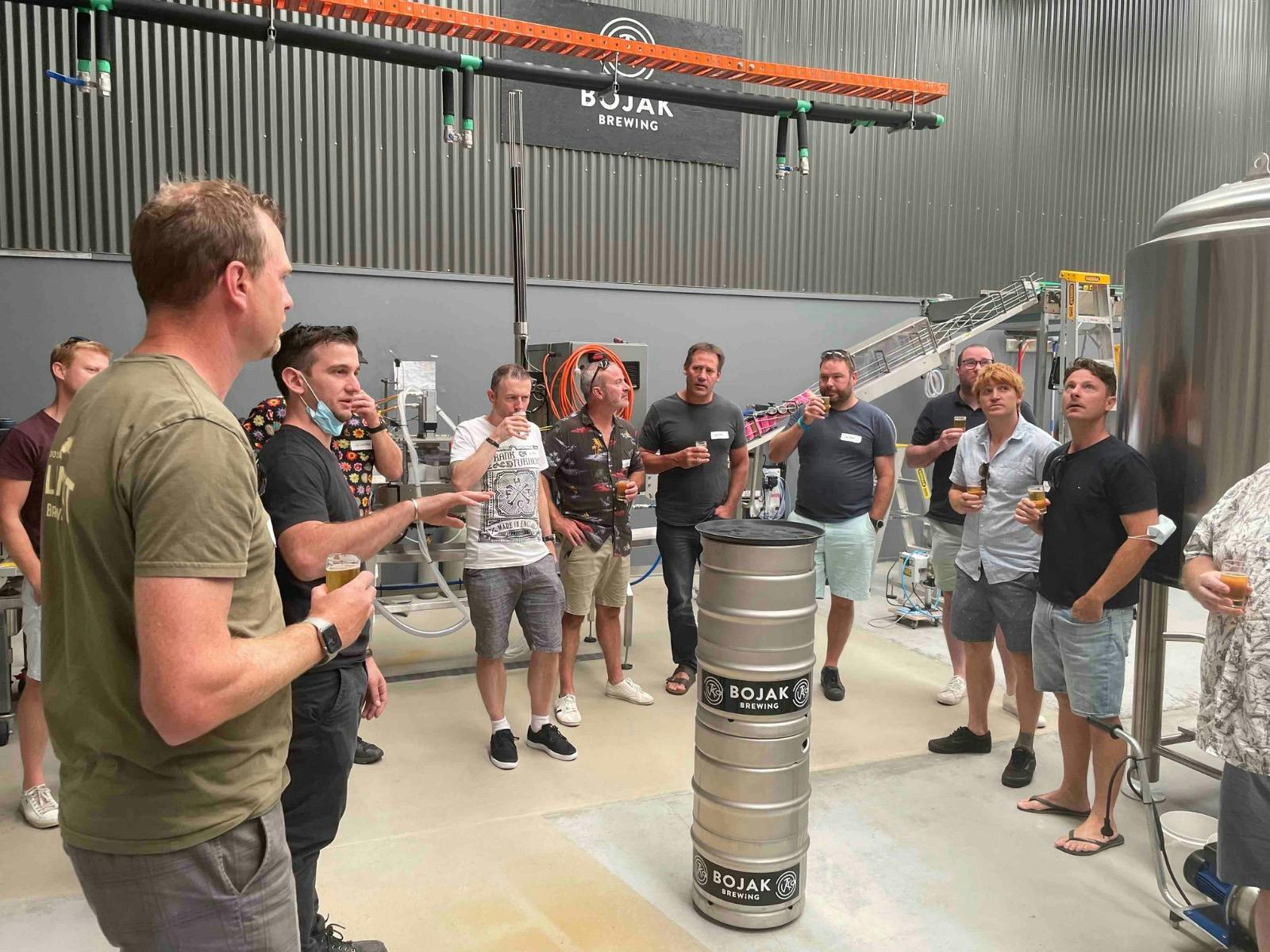 A group of people standing in a semi circle listening to a brewer talk about the brewing process